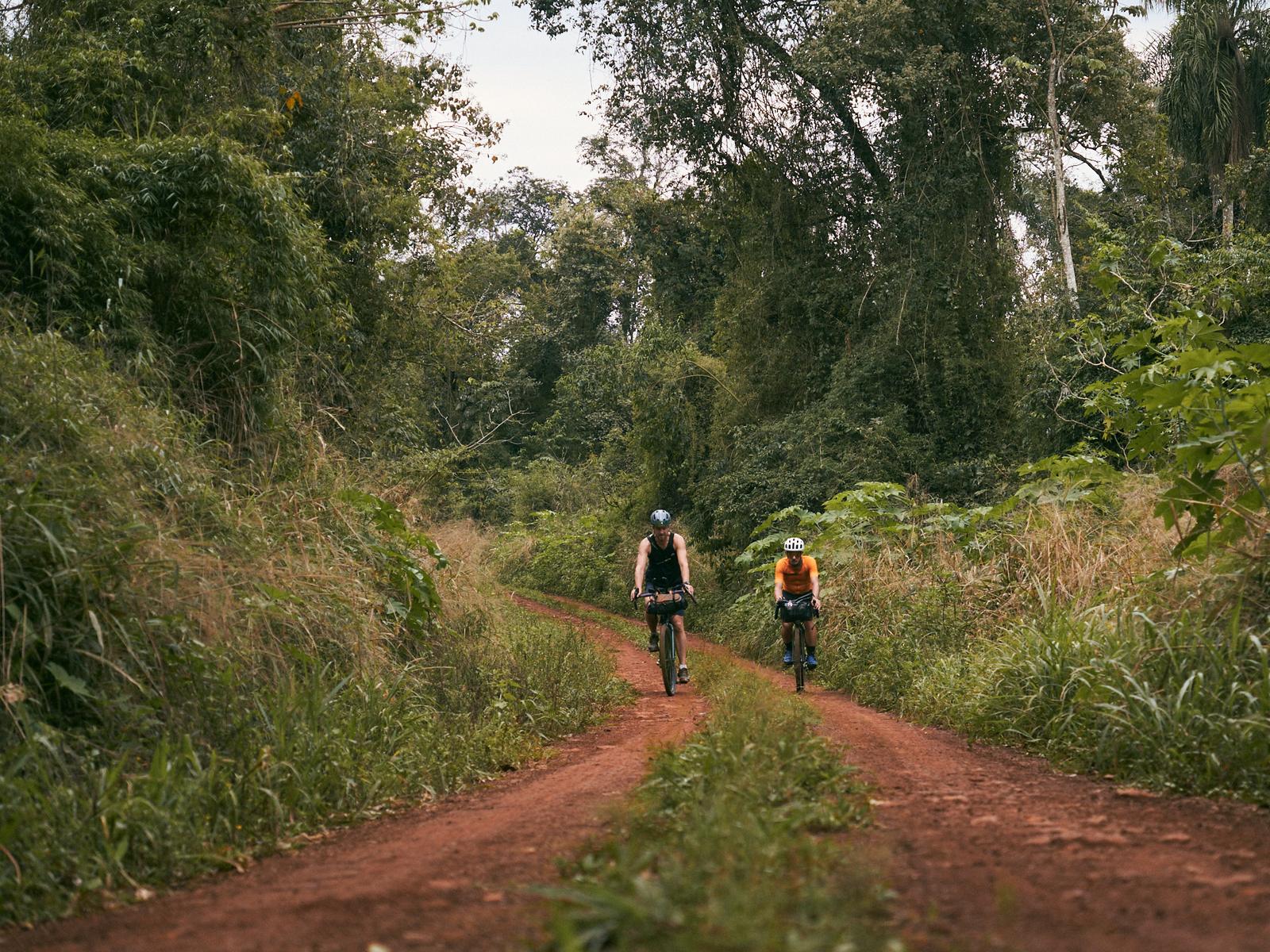 Two riders on a red dirt track through the Misiones jungle
