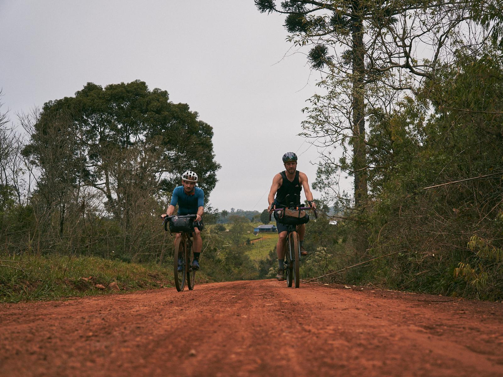 Two riders coming up a red dirt road in Misiones