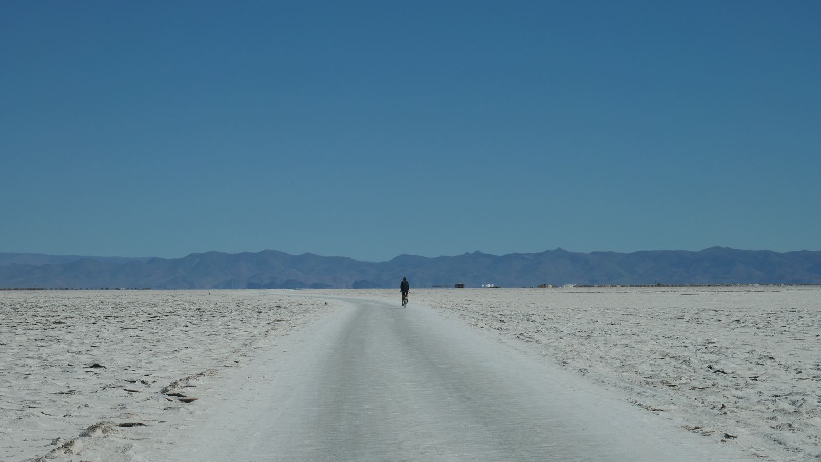 A lone rider on a white road across the Salinas Grandes salt flat
